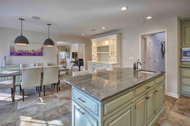 kitchen featuring hanging light fixtures, sink, an island with sink, and dark stone countertops