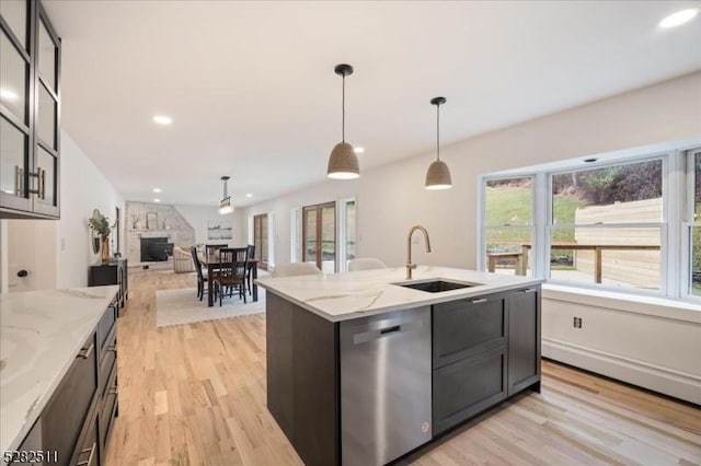 kitchen with light stone countertops, dishwasher, sink, hanging light fixtures, and a kitchen island with sink