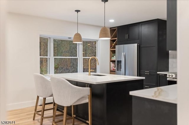 kitchen with light stone countertops, decorative light fixtures, stainless steel appliances, light hardwood / wood-style floors, and sink