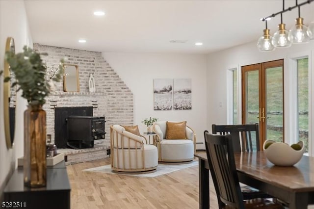 dining room with a wood stove, a baseboard radiator, light hardwood / wood-style flooring, and french doors