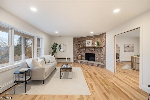 living room featuring a brick fireplace, baseboard heating, and light hardwood / wood-style floors