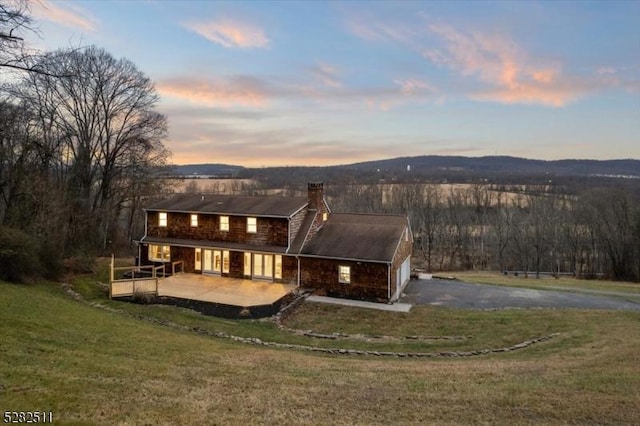 back house at dusk featuring a patio area, a mountain view, and a lawn