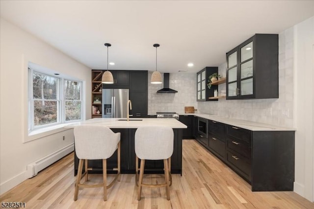 kitchen with appliances with stainless steel finishes, decorative backsplash, a kitchen island with sink, decorative light fixtures, and wall chimney exhaust hood