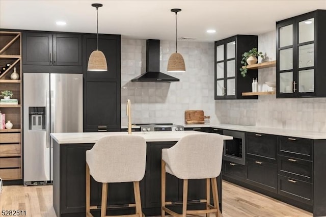 kitchen featuring stainless steel fridge, a breakfast bar area, light wood-type flooring, built in microwave, and wall chimney range hood