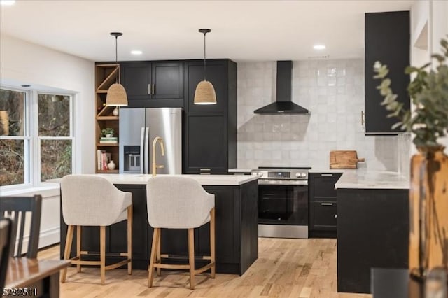 kitchen featuring a kitchen bar, appliances with stainless steel finishes, decorative backsplash, hanging light fixtures, and wall chimney exhaust hood