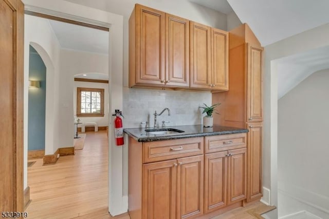 kitchen featuring lofted ceiling, sink, light hardwood / wood-style flooring, dark stone countertops, and backsplash