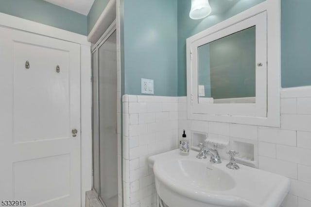 bathroom featuring a shower with door, sink, and tile walls