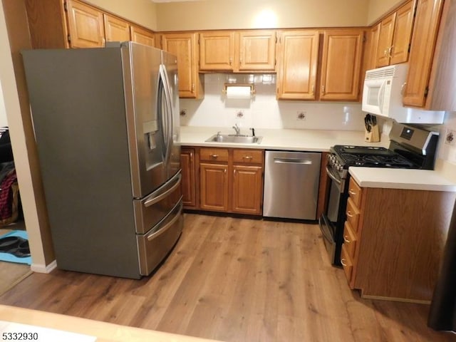 kitchen featuring light wood finished floors, stainless steel appliances, light countertops, and a sink