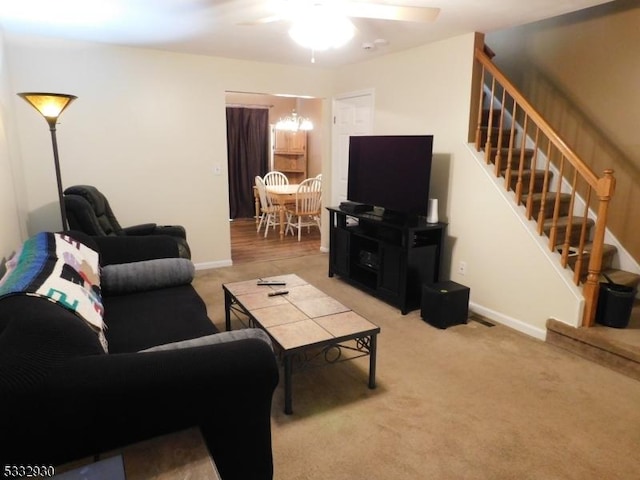 living room featuring light colored carpet, a ceiling fan, stairs, and baseboards