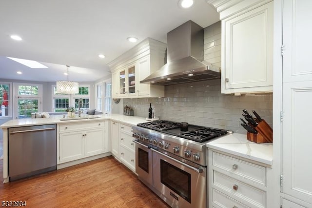 kitchen featuring kitchen peninsula, white cabinets, wall chimney exhaust hood, and stainless steel appliances