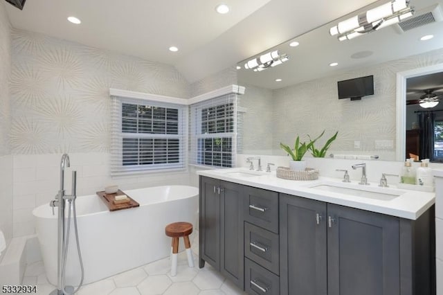 bathroom with a tub to relax in, vanity, tile walls, and ceiling fan