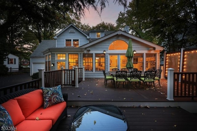 back house at dusk featuring a garage, a deck, and an outdoor living space