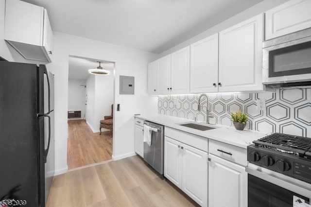 kitchen with stainless steel appliances, light wood-type flooring, sink, white cabinetry, and backsplash