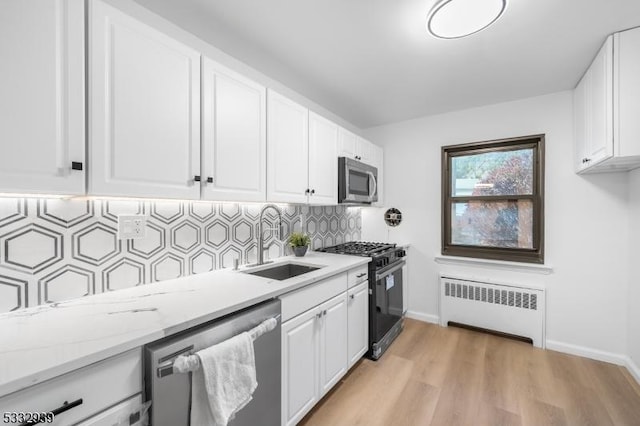 kitchen with sink, white cabinets, light stone counters, radiator heating unit, and appliances with stainless steel finishes