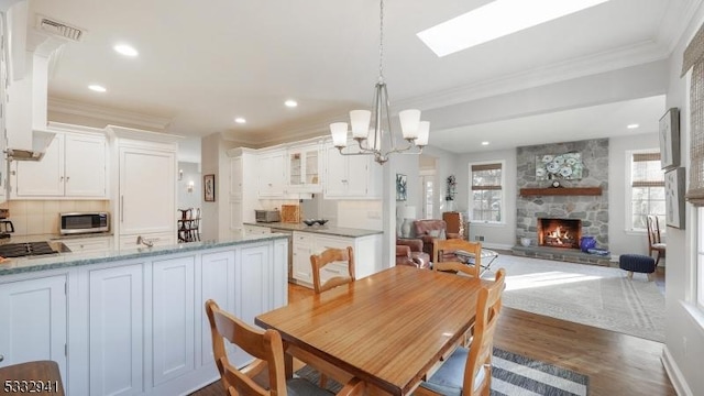 dining space with a fireplace, a notable chandelier, dark hardwood / wood-style floors, a skylight, and ornamental molding