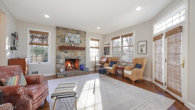 sitting room with a wealth of natural light, dark hardwood / wood-style floors, and a stone fireplace