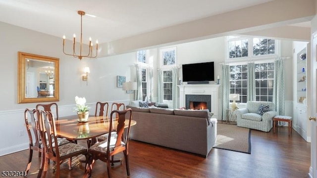 dining room featuring dark wood-type flooring, a chandelier, and a tiled fireplace