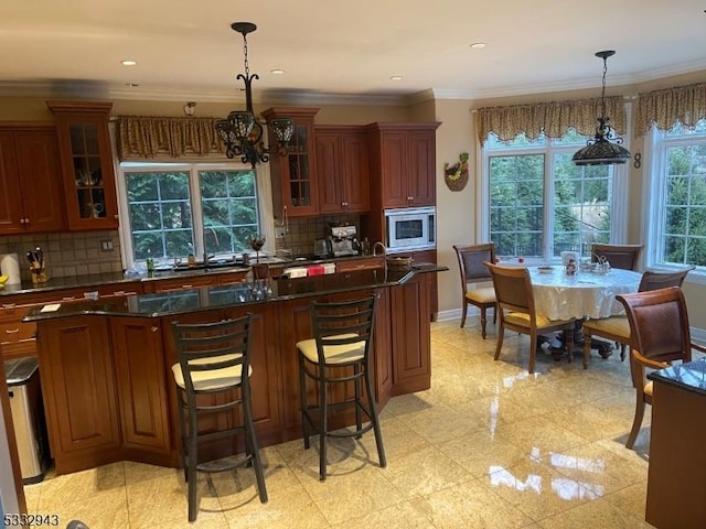 kitchen with stainless steel microwave, hanging light fixtures, an inviting chandelier, backsplash, and ornamental molding