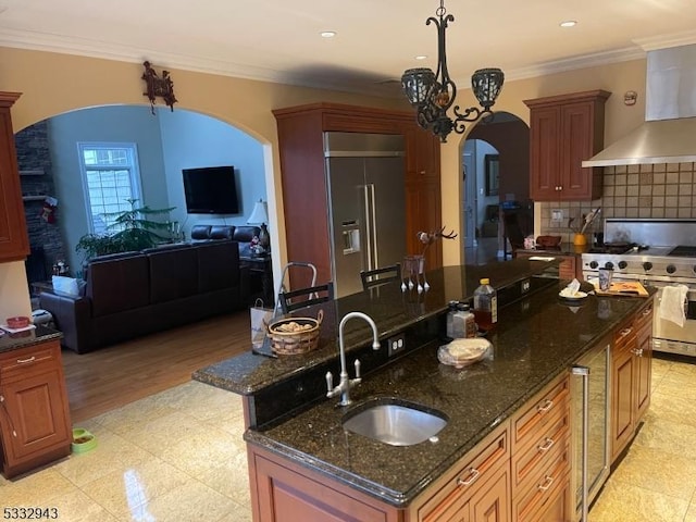 kitchen with sink, high quality appliances, ornamental molding, and wall chimney exhaust hood