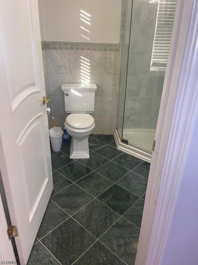 bathroom with toilet, tile patterned flooring, tile walls, and a shower with shower door