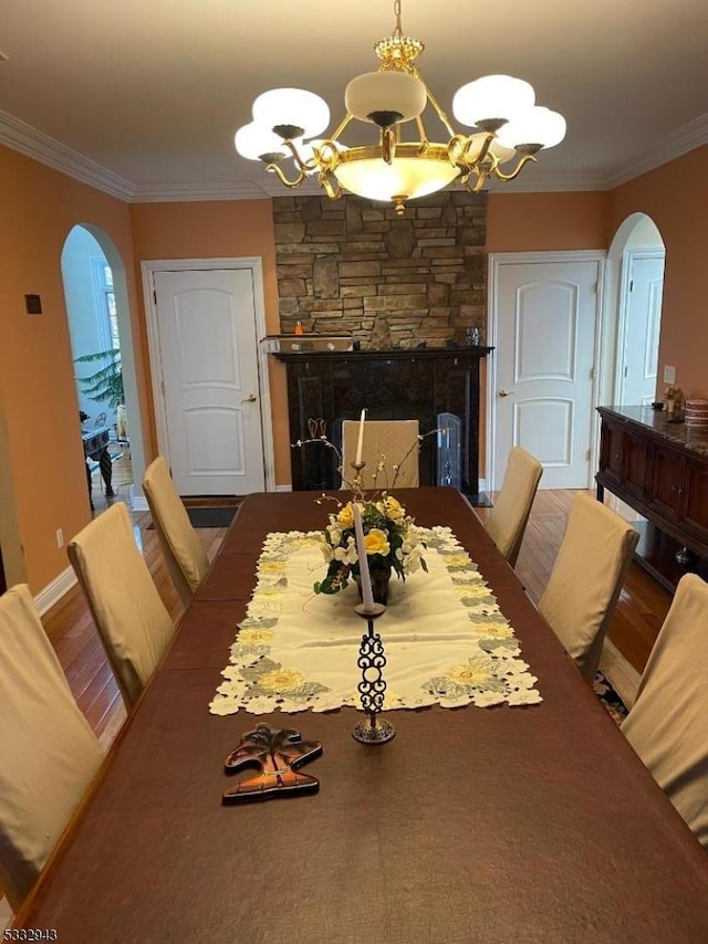 dining area featuring an inviting chandelier, crown molding, and a stone fireplace