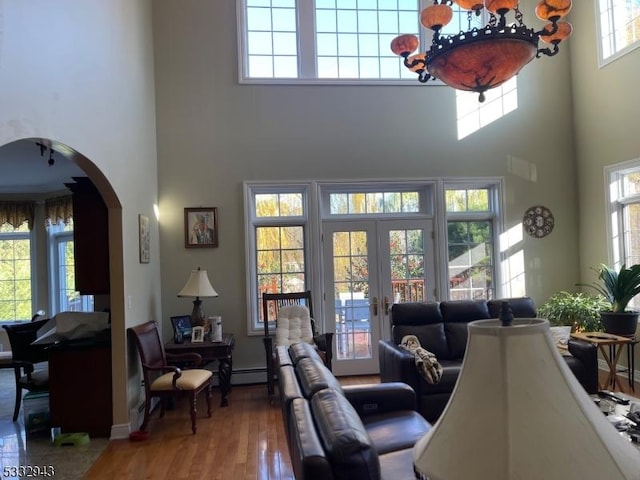 living room with baseboard heating, french doors, a towering ceiling, and wood-type flooring