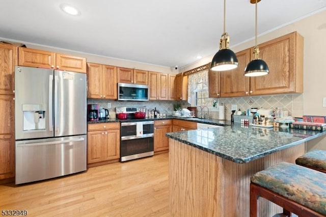 kitchen featuring a kitchen bar, kitchen peninsula, stainless steel appliances, hanging light fixtures, and dark stone counters