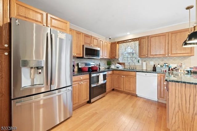 kitchen with decorative light fixtures, stainless steel appliances, dark stone countertops, decorative backsplash, and light wood-type flooring