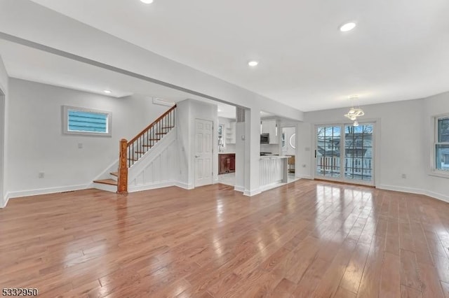 unfurnished living room featuring an inviting chandelier and light hardwood / wood-style floors