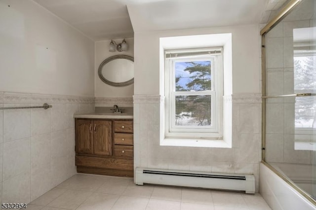 bathroom with combined bath / shower with glass door, tile walls, baseboard heating, tile patterned flooring, and vanity