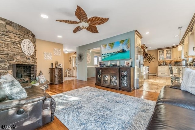 living room featuring ceiling fan, a stone fireplace, and light wood-type flooring