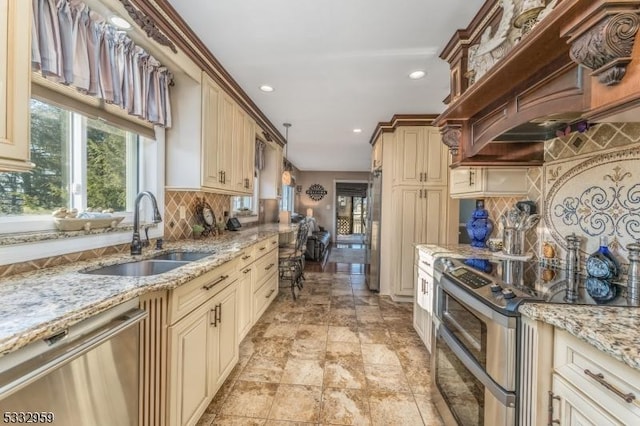 kitchen featuring light stone countertops, appliances with stainless steel finishes, sink, backsplash, and cream cabinetry