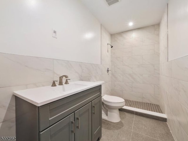 bathroom featuring tiled shower, tile walls, toilet, tile patterned floors, and vanity