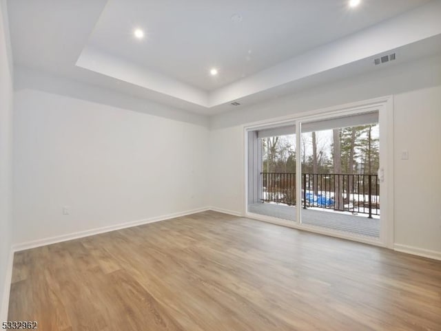 empty room with a tray ceiling and light hardwood / wood-style flooring