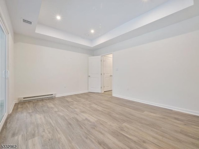 unfurnished room featuring light hardwood / wood-style floors, a baseboard heating unit, and a tray ceiling