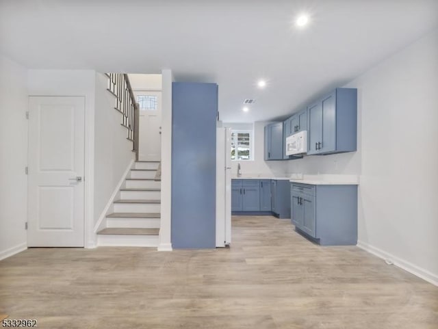 kitchen featuring white appliances, light hardwood / wood-style floors, and blue cabinetry