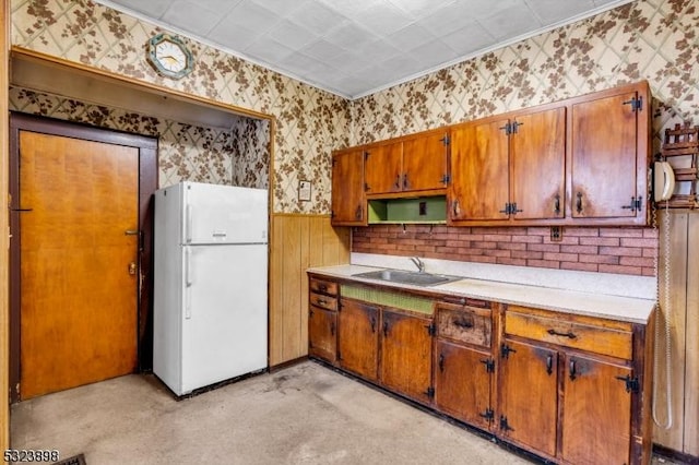 kitchen with sink, wood walls, white fridge, and ornamental molding