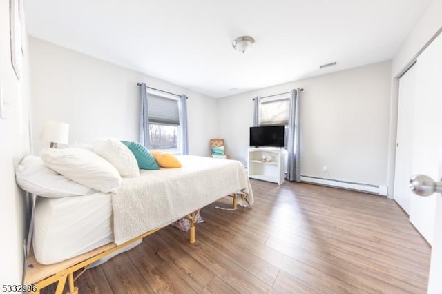 bedroom with a closet, hardwood / wood-style floors, and baseboard heating