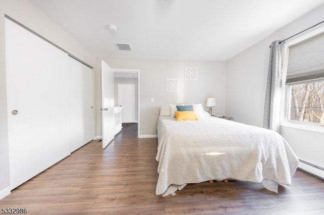 bedroom with a closet, hardwood / wood-style flooring, and baseboard heating