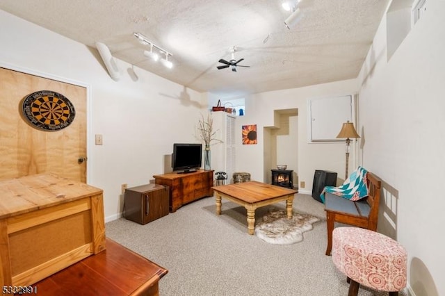 carpeted living room featuring ceiling fan, a wood stove, a textured ceiling, and rail lighting