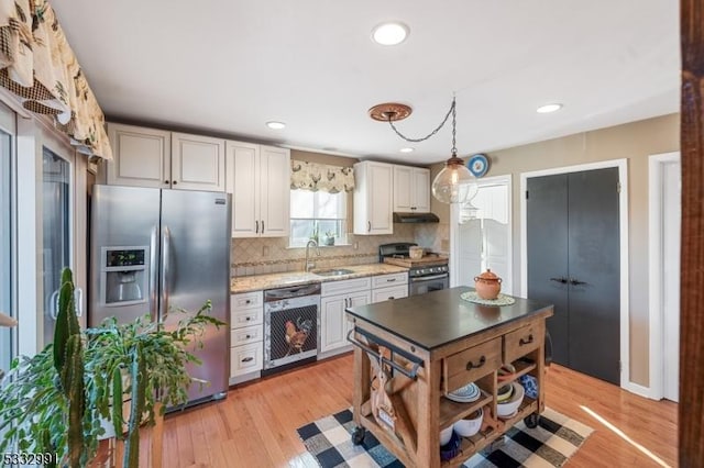 kitchen featuring stainless steel appliances, decorative backsplash, sink, hanging light fixtures, and light wood-type flooring