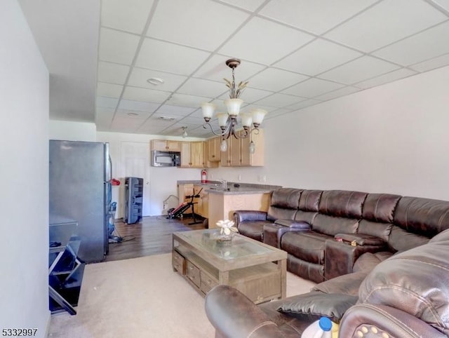 living room with sink, light wood-type flooring, an inviting chandelier, and a drop ceiling