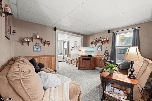 carpeted living room featuring a drop ceiling and wooden walls