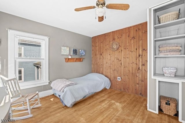 bedroom featuring wood walls, ceiling fan, hardwood / wood-style floors, and multiple windows