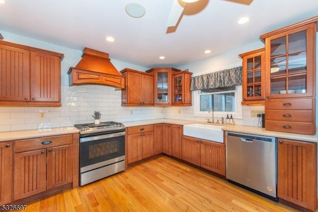 kitchen featuring ceiling fan, premium range hood, sink, light hardwood / wood-style flooring, and stainless steel appliances