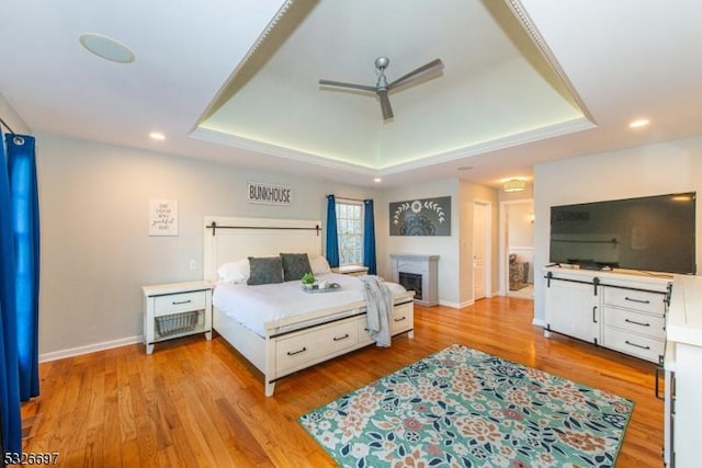 bedroom with ceiling fan, light hardwood / wood-style floors, and a tray ceiling