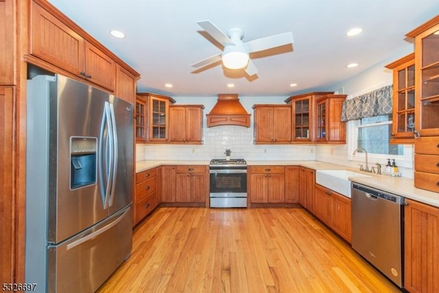 kitchen featuring custom exhaust hood, stainless steel appliances, sink, backsplash, and light hardwood / wood-style flooring