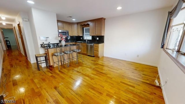 kitchen with backsplash, light wood-type flooring, a breakfast bar, and appliances with stainless steel finishes