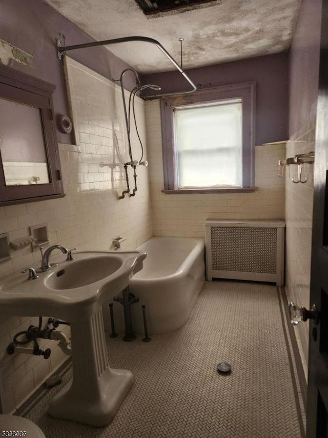 bathroom with tile patterned floors, radiator, tile walls, and a textured ceiling