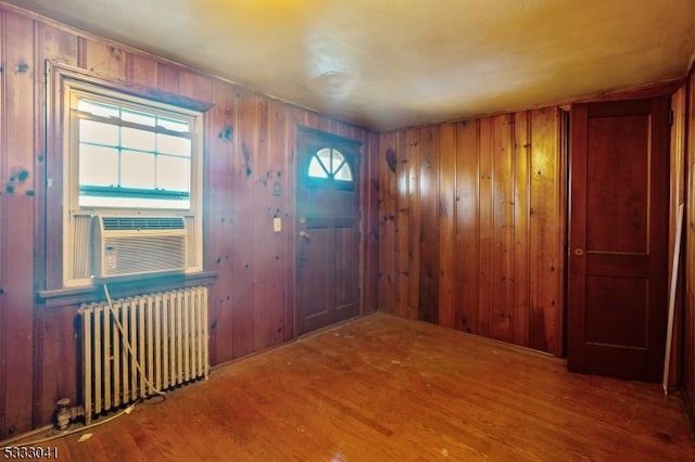 foyer entrance with wood-type flooring, wooden walls, radiator heating unit, and cooling unit